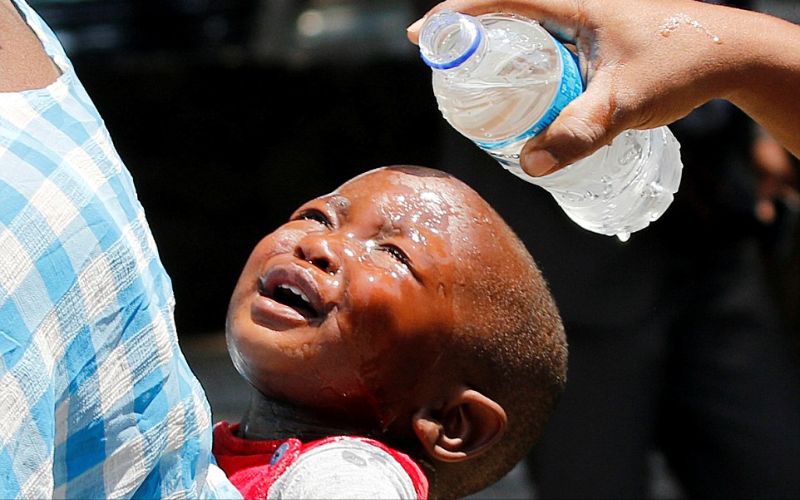 إمرأة تسكب الماء على رأس طفل تعرض للغاز المسيل للدموع أثناء مواجهات بين الشرطة والباعة في زمبابوي.سبتمبر