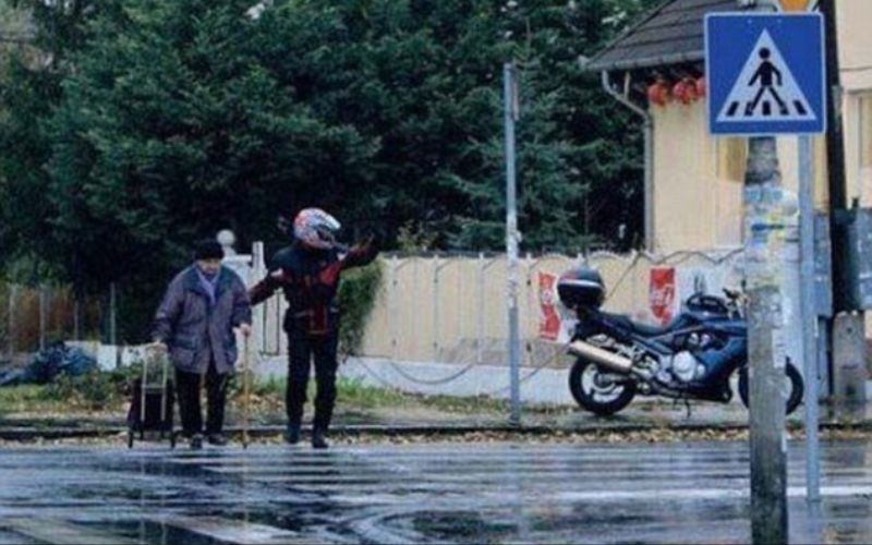 رجل قطع طريقه وركن دراجته لمساعدة عجوز بقطع الطريق في يوم ماطر