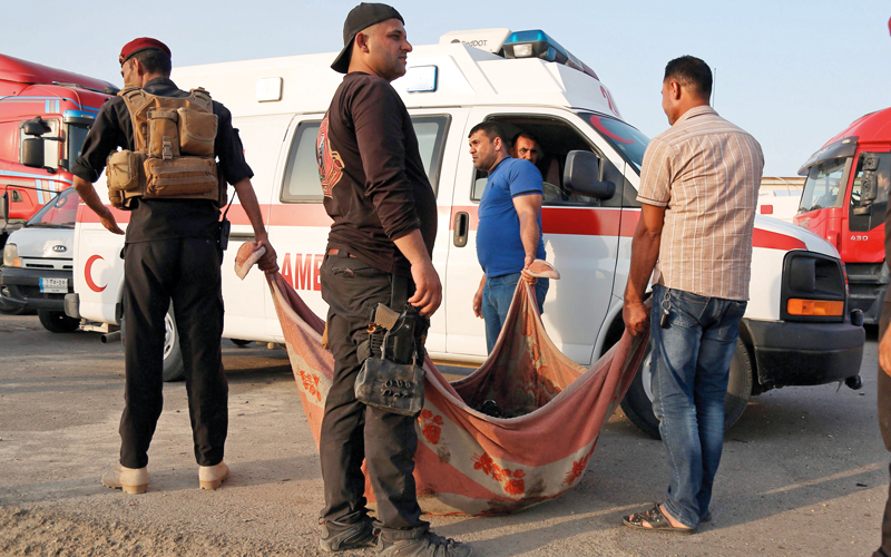 عناصر من قوات الأمن يحملون جثة أحد ضحايا هجوم الناصرية.   أ.ف.ب