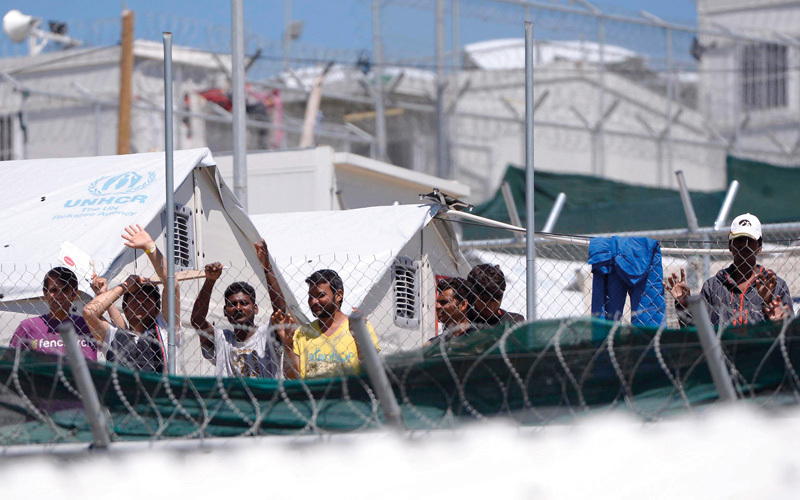 المهاجرين واللاجئين يقفون خلف سياج من الاسلاك الشائكة في معسكر موريا، ايي بي ايه