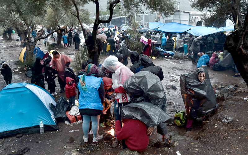 مهاجرون تحت الأمطار الغزيرة يقفون خارج مكتب تسجيل موريا. أ.ف.ب