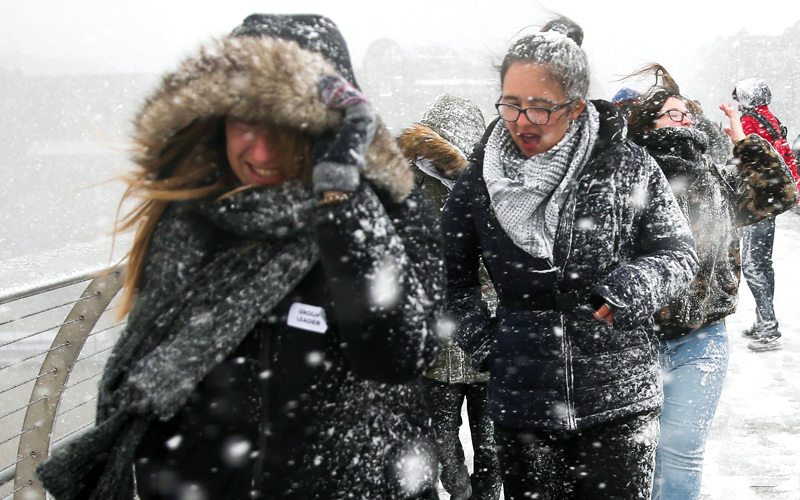 مشاة يعبرون جسر الألفية مع تساقط كثيف للثلوج في لندن. أ.ف.ب