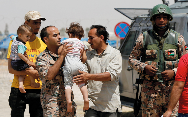 جندي أردني يحمل طفلاً سورياً من النازحين عند الحدود مع سورية.      رويترز
