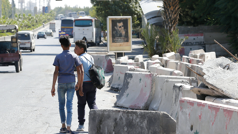 سوريون يمرّون قبالة الكتل الأسمنتية التي تمت إزالتها من الشوارع الرئيسة.  أ.ف.ب