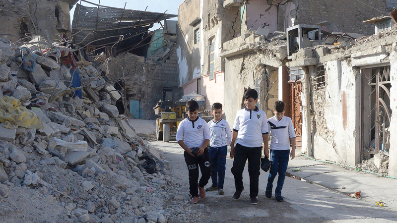 أطفال عراقيون في طريقهم إلى المدرسة وسط مباني الموصل المهدمة بعد تحريرها من «داعش». أ.ف.ب