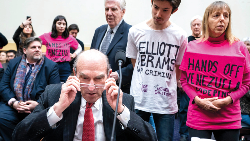 إليوت أبرامز في مواجهة مجموعة من المتظاهرين خلال تقديم شهادته أمام لجنة الشؤون الخارجية بالكونغرس.  إي.بي.إيه