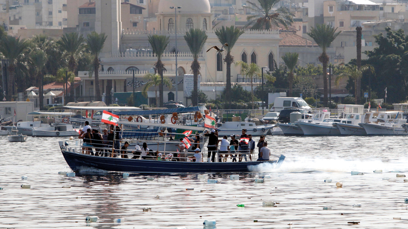 متظاهرون يلوحون بالأعلام اللبنانية على متن قارب بمدينة طرابلس الساحلية أمس. أ.ف.ب