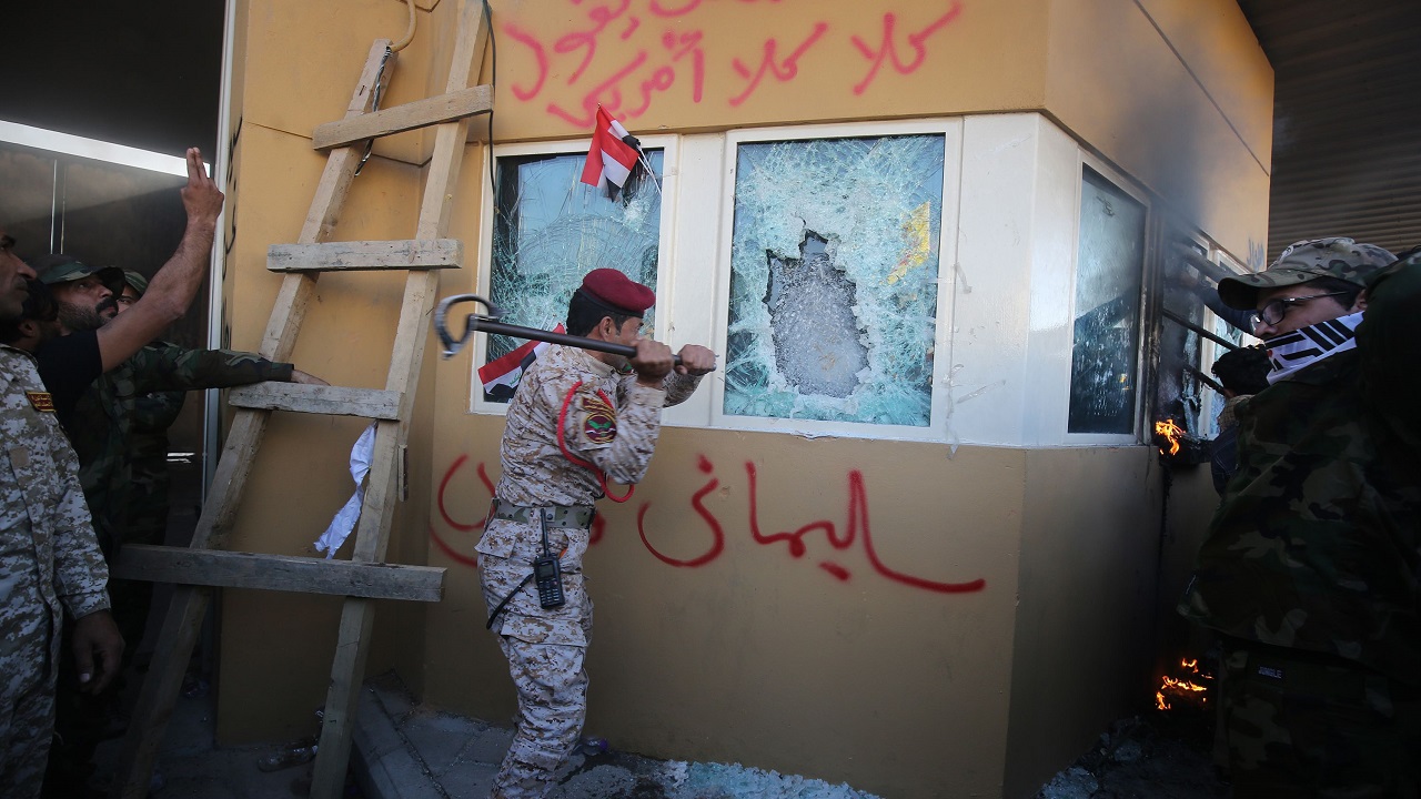 عنصر من «الحشد الشعبي» يحطم زجاج السفارة المضاد للرصاص، وآخرون كتبوا على الحائط «سليماني قائدي»، في إشارة إلى قائد «فيلق القدس» في «الحرس الثوري الإيراني»، قاسم سليماني. (أ. ف. ب)