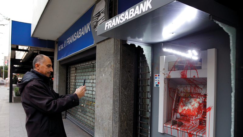 مواطن لبناني يصوّر التلف الذي لحق بجهاز الصراف الآلي. أ.ب