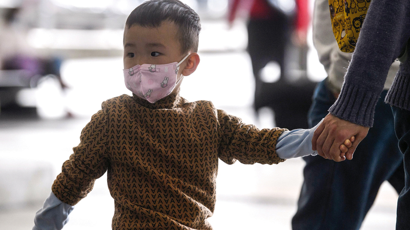 طفل يضع قناعاً واقياً وهو ممسك بيد أبيه في مطار هونغ كونغ.  أ.ف.ب