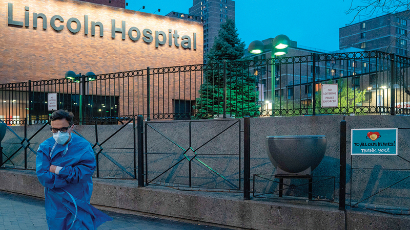 عضو في فريق طبي يقف إلى جانب لافتة كتب عليها عبارة شكر للعاملين في الرعاية الصحية بمستشفى لينكولون. أ.ف.ب