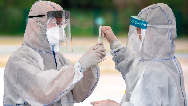 فنيا مختبرات بالملابس الواقية يعرضان عينة لعاب بمنشأة اختبار لـ«كورونا» في برلين.	 أ.ف.ب