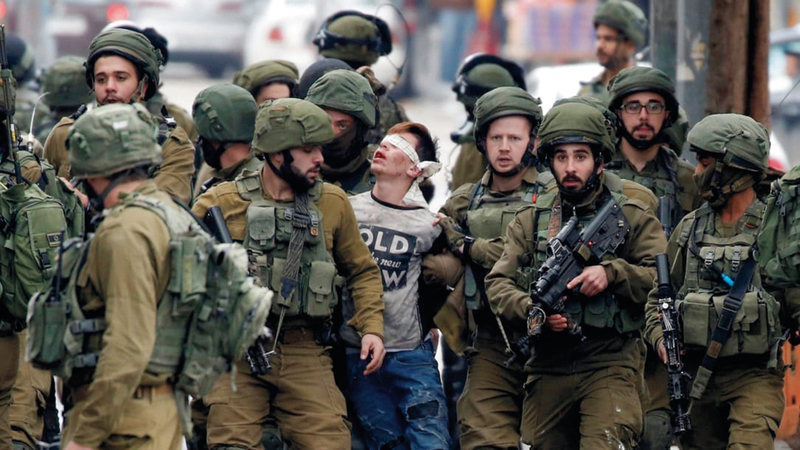حشد من الجنود الإسرائيليين يعتقلون طفلاً فلسطينياً بعد تعصيب عينيه وضربه. من المصدر