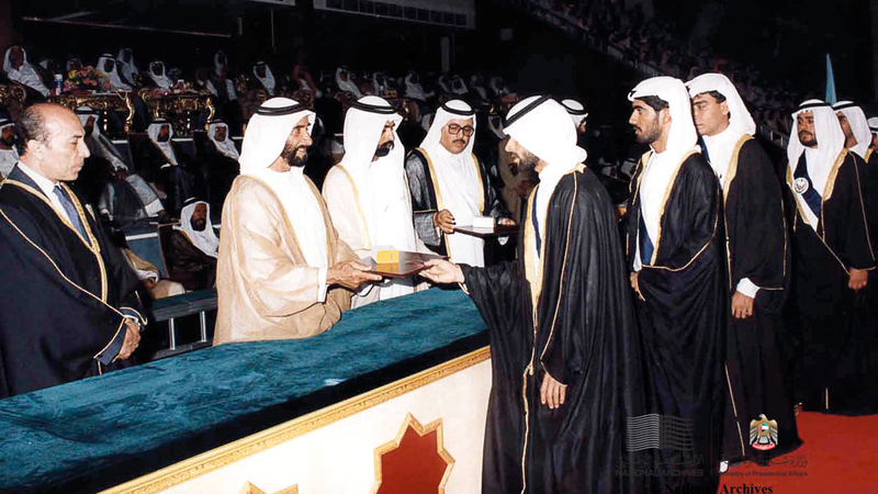 الشيخ زايد بن سلطان آل نهيان أثناء توزيع شهادات التخرج لطلاب جامعة الإمارات وبجانبه الشيخ نهيان بن مبارك آل نهيان.   (الأرشيف الوطني)