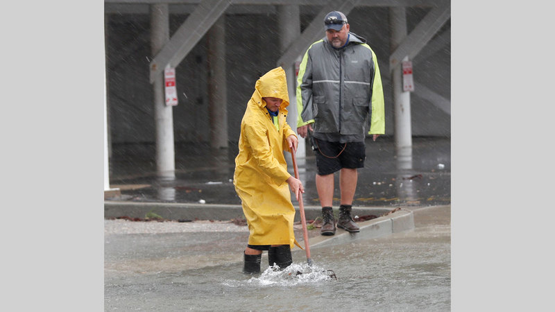 عاملان يحاولان فتح بالوعات تصريف المياه التي أغلقتها المخلفات التي حملتها مياه الفيضان. أ.ف.ب