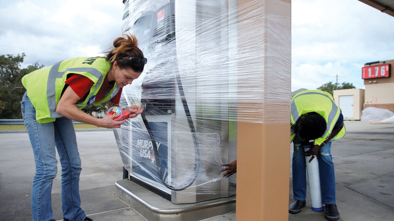 عاملان في محطة وقود يلفان المضخة بالنايلون حتى يحميانها من المواد التي ربما تحملها رياح الإعصار في المسيسبي. رويترز