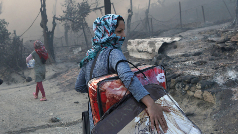 لاجئة تحمل متعلقاتها بعد أن شبّ حريق بمخيم لاجئين بجزيرة ليسبوس اليونانية في سبتمبر 2020.  رويترز