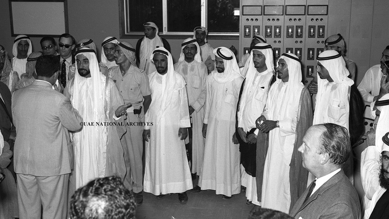 الشيخ زايد يستمع إلى مدرس يقدم مشروعاً يتعلق بالكهرباء الساكنة خلال افتتاح المعرض السنوي الأول بمدرسة الكندي الابتدائية في أبوظبي يوم 24 أبريل 1971. الأرشيف الوطني