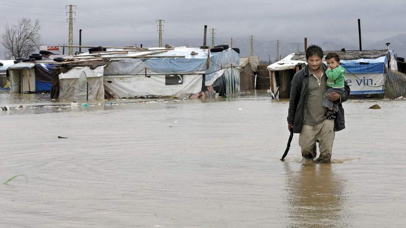 لاجئ يشق طريقه وسط المياه والأوحال جراء الأمطار الغزيرة التي دمرت المخيم الذي يعيش فيه.   أ.ب