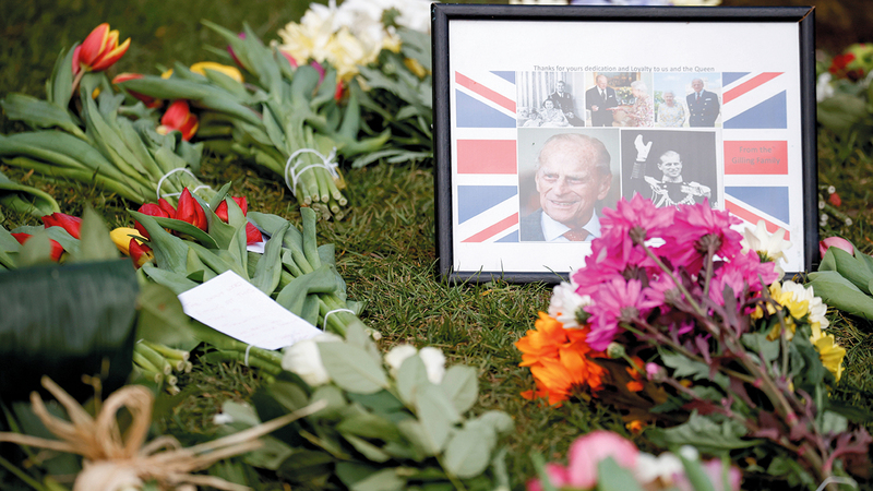 لوحة تضم صوراً عدة لزوج الملكة إضافة إلى باقات ورد وضعت عند سور قصر باكينغهام من قبل البريطانيين الذين هبوا لمواساة العائلة الملكية في فقيدها.  رويترز