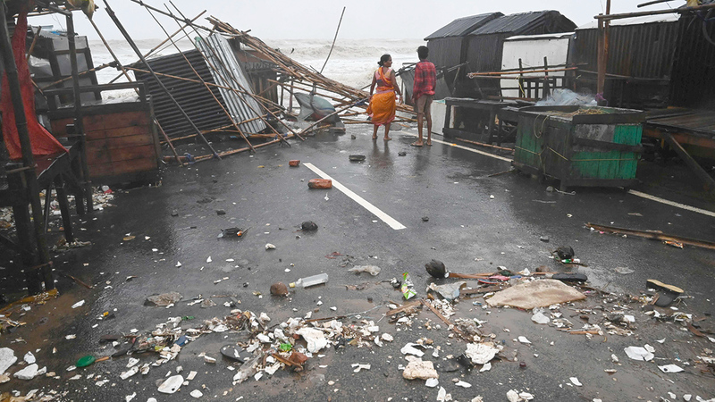 مواطنان هنديان يراقبان مياه البحر الهائجة وسط الحطام.   أ.ف.ب