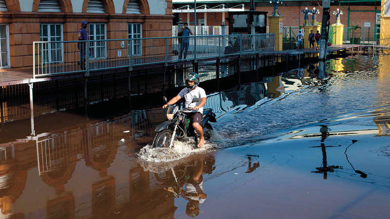 يقود دراجته النارية وسط مياه الفيضان.  أ.ف.ب