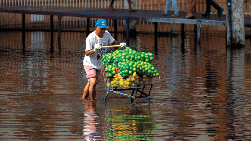 يواجه صعوبة في تحريك عربته المملوءة بالفواكه وسط شارع غمرته المياه.  	 أ.ف.ب