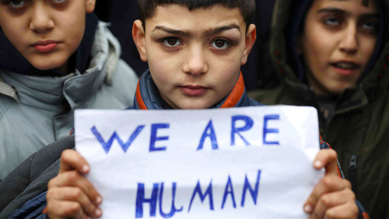 «نحن بشر» لافتة حملها طفل مهاجر عالق على الحدود ما بين بيلاروسيا وبولندا.   رويترز