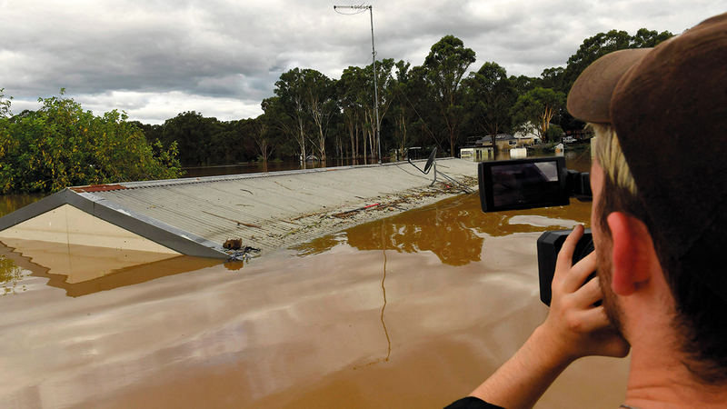 رجل يلتقط صوراً لمنزل غمرته مياه الفيضان على ضفة نهر هوكسبيري في ضاحية وينسور بمدينة سيدني. أ.ف.ب