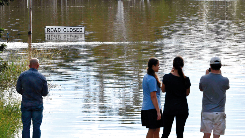 عدد من الأشخاص يلقون نظرة فاحصة على المياه الفائضة لنهر هوكسبيري في ضاحية وينسور بمدينة سيدني.   أ.ف.ب
