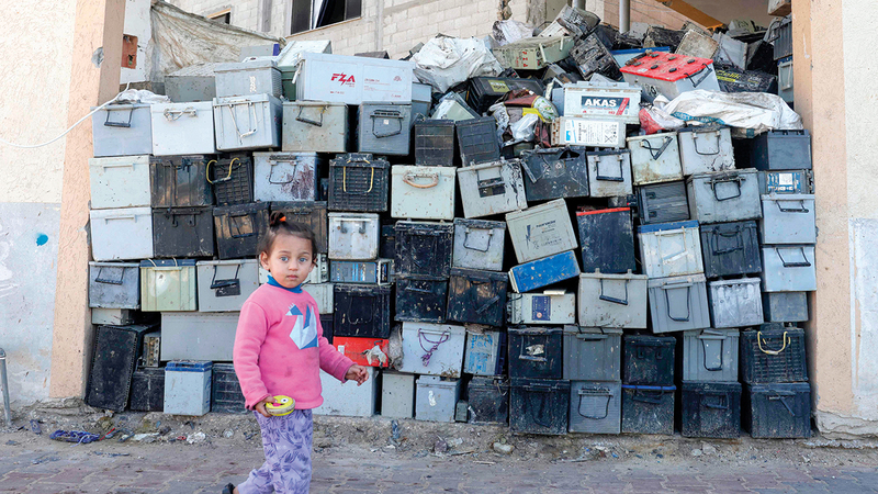 طفلة فلسطينية تمر قبالة كومة من البطاريات المستعملة التي تحتاج إلى التخلص منها.   أ.ف.ب