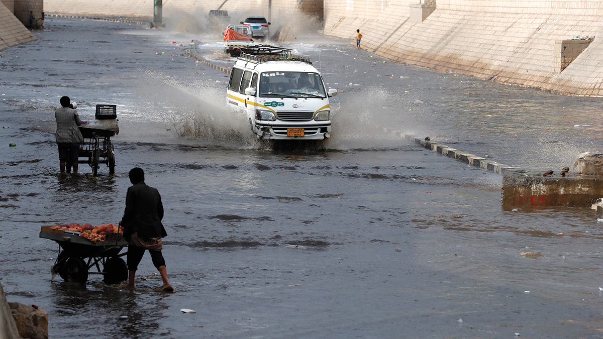 بائع فواكه متجوّل يجر عربته وسط مياه الأمطار التي غطت شوارع مدن يمنية عدة.  إي.بي.إيه