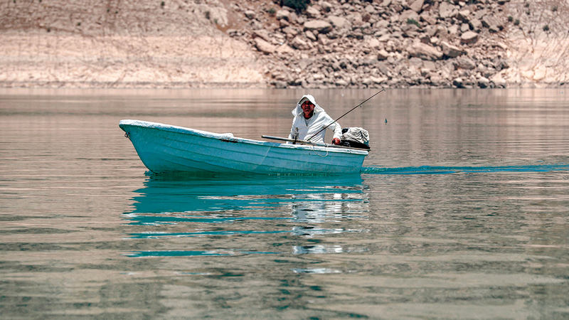 صياد سمك يُبحر بقاربه وسط مياه ضحلة بالقرب من سد دوكان.  أ.ف.ب
