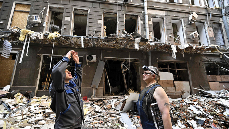 عاملان يقفان في فناء بين الأنقاض بعد قصف روسي على مجمع تجاري في خاركيف. أ.ف.ب