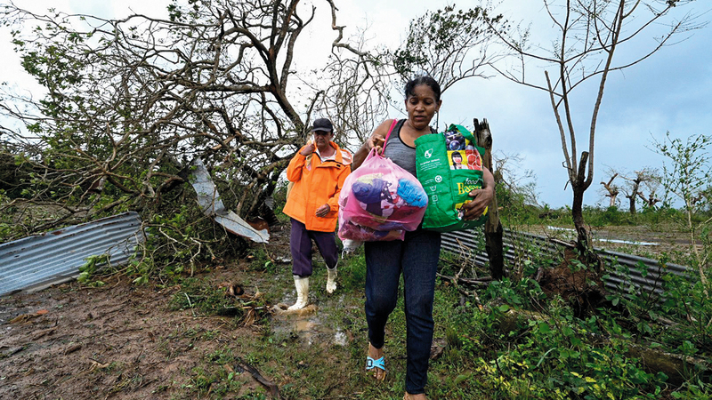 سيدة كوبية وزوجها يحملان بعض أغراضهما بعد أن هدم بيتهما جرّاء الريح الشديد والمطر غرب كوبا. أ.ف.ب