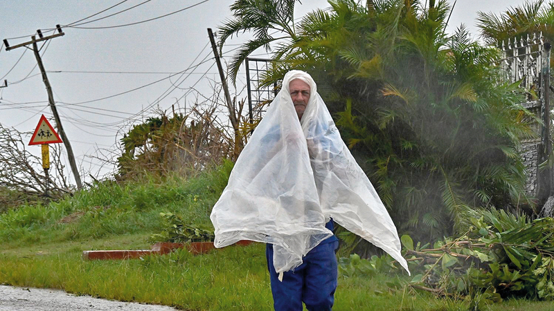 رجل يحاول حماية نفسه بغطاء بلاستيكي من الرياح والمطر. أ.ف.ب