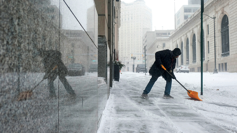 رجل يحاول إزالة الثلج من الرصيف في وسط مدينة ديترويت بسبب العاصفة الشتوية.   أ.ف.ب