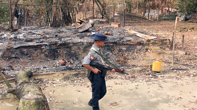 ضابط أمن من ميانمار يمر قبالة عدد من بيوت مسلمي الروهينغا التي تم حرقها.   أ.ب