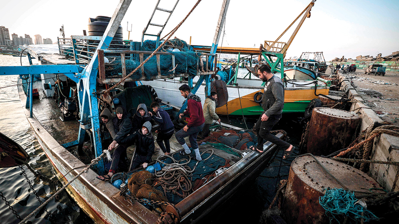 جهاد الهسي وأبناؤه يعملون على قاربهم في ميناء غزة. 	  أ.ف.ب