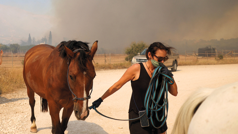 امرأة تغادر مع فرسها جراء حريق هائل بالقرب من أثينا.  رويترز