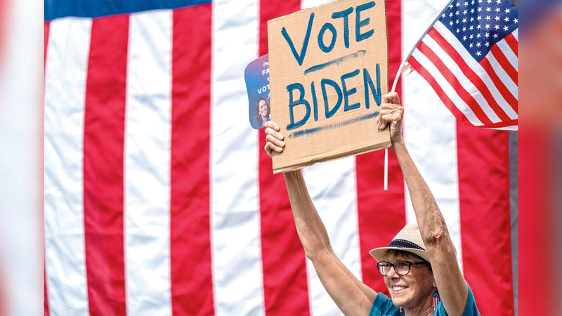 أميركية ترفع لافتة تدعو إلى التصويت لبايدن.   أ.ف.ب