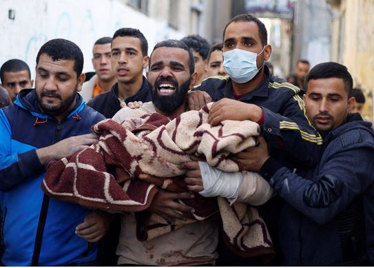 رجل فلسطيني يحمل طفلا مصابا في موقع الغارات الإسرائيلية على المنازل في رفح