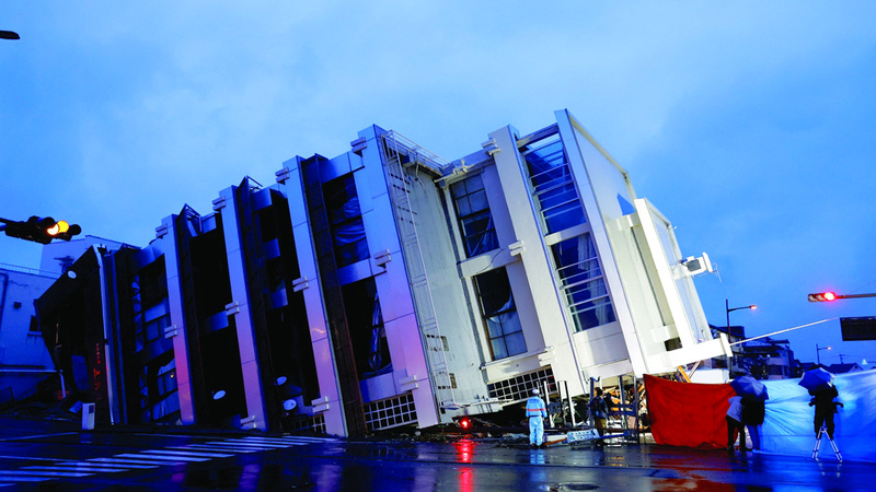 أناس يقفون بالقرب من بناية منهارة في مدينة واجيما. رويترز