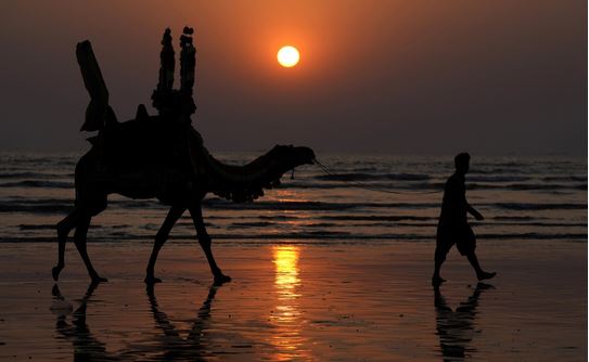 صورة لرجل باكستاني وجمله عند غروب الشمس الأخير لعام 2023 على شاطئ كليفتون في كراتشي، باكستان