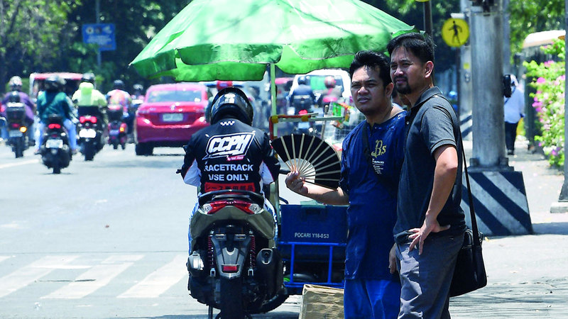 أحد المشاة في العاصمة الفلبينية يقاوم حرارة الطقس بمروحة. أ.ف.ب