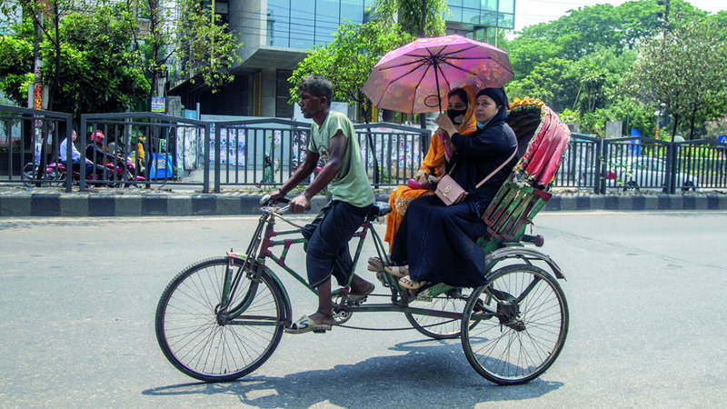 يحملون مظلات للاتقاء من حرارة الشمس أثناء ركوبهم الدرّاجة. إي.بي.ايه