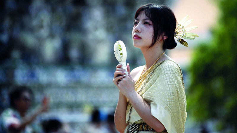 سائحة صينية تستخدم مروحة تعمل بالبطارية بالقرب من معبد دون في العاصمة التايلاندية بانكوك. إي.بي.إيه