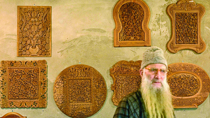 Wood carving artisan Ghulam Nabi Dar stands beside designs crafted on a wooden piece, at his workshop in Srinagar on February 18, 2025. (Photo by Tauseef MUSTAFA / AFP)