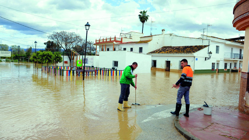 رجال ينظفون الشارع أمام منازلهم بعد هطول أمطار غزيرة. رويترز