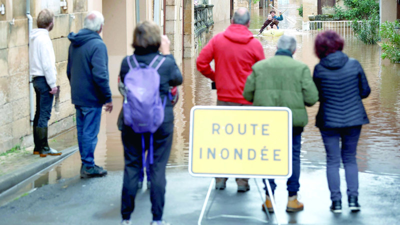 أشخاص يقفون خلف لافتة &laquo;طريق مغمور بالمياه&raquo;. أ.ف.ب